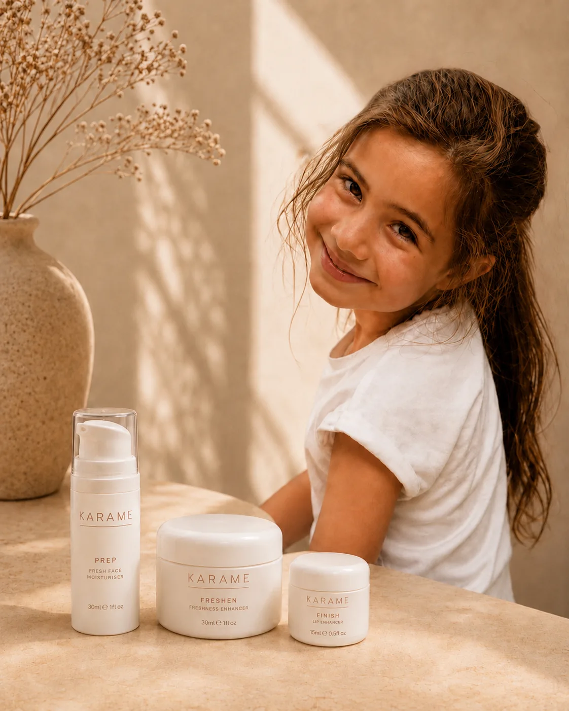 A young girl smiling beside the three KARAME products on a sunlit table